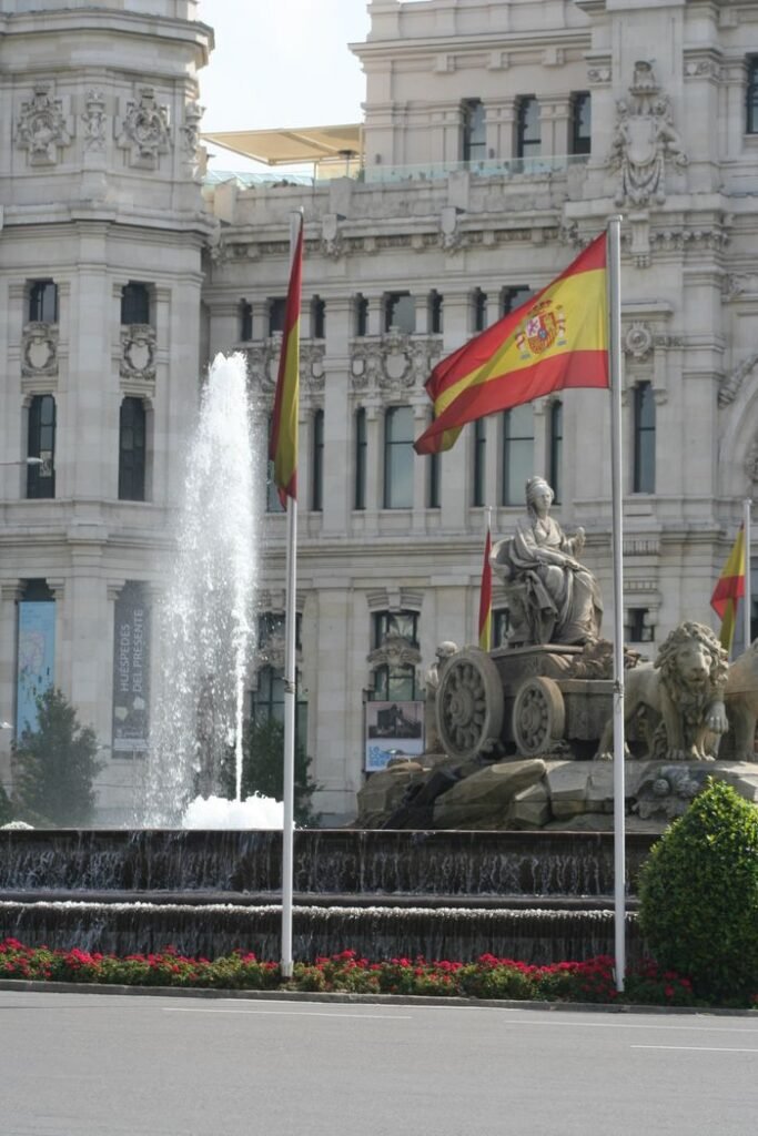 Cibeles Fountain with Spanish flags in Madrid, showcasing neoclassical architecture.